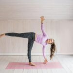 Woman practicing yoga pose indoors on a pink mat, balancing gracefully.
