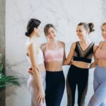 Four women in activewear smiling and enjoying fitness indoors, promoting health and togetherness.
