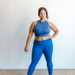 A confident woman poses in blue activewear indoors, promoting body positivity and self-love.